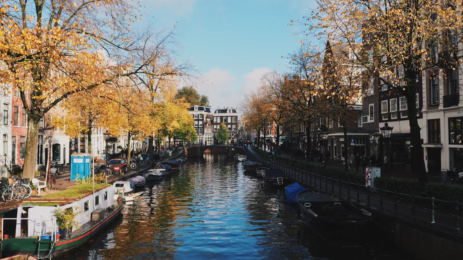 Canal d'Amsterdam bordé d'arbres aux couleurs d'automne, bateaux amarrés le long du quai