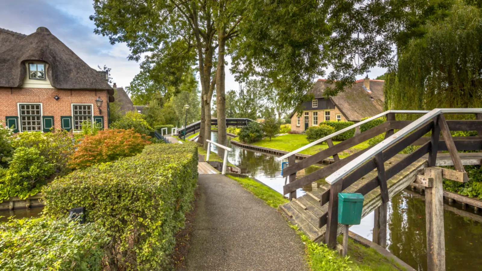 Maisons au toit de chaume, sentier et petit pont de bois au bord d'un canal à Giethoorn