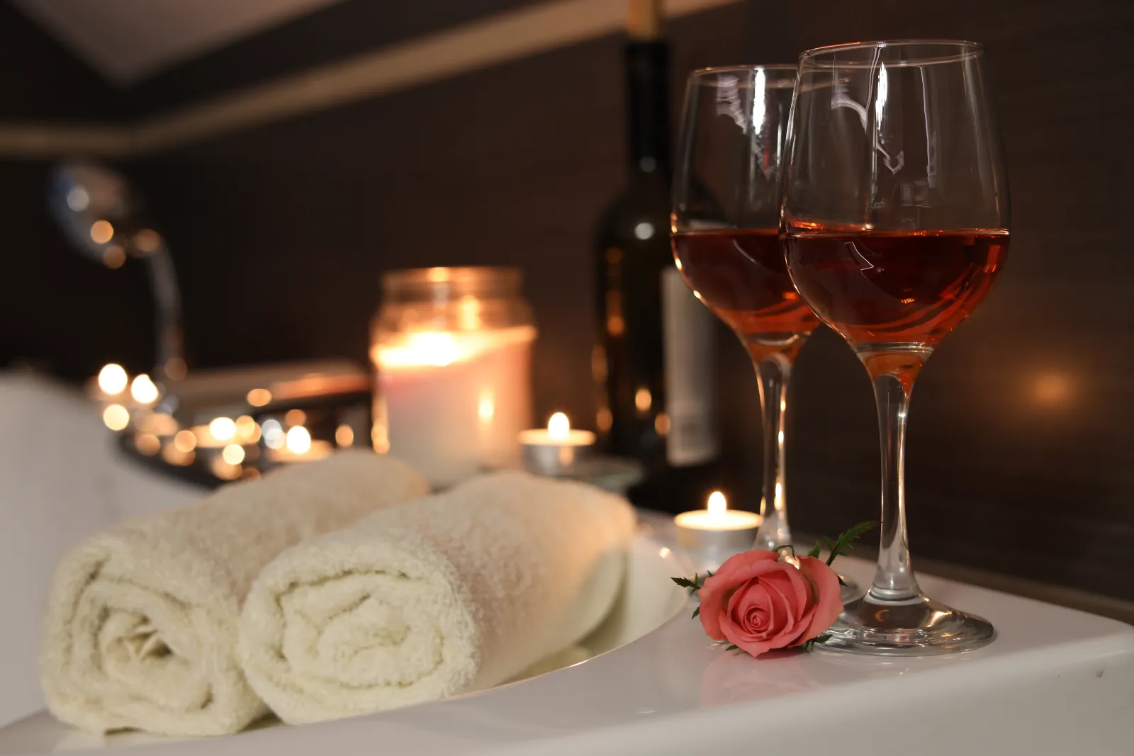 Deux verres de vin, des bougies et une rose posés sur le rebord d'une baignoire, serviettes roulées