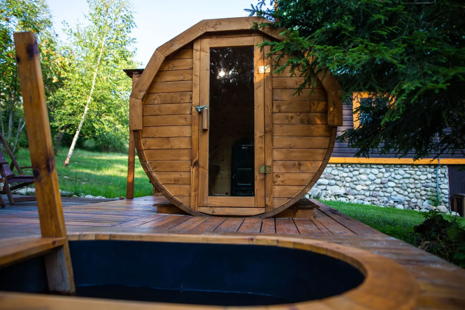 Sauna tonneau en bois sur une terrasse, bassin d'eau froide au premier plan